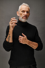 attractive fashionable mature man with beard in chic black turtleneck posing and looking at camera