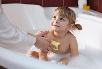 Mother washing her little daughter with sponge in bathtub, closeup