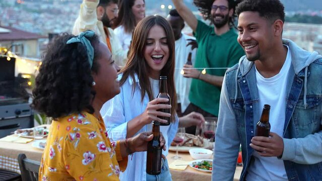 Multiethnic friends toasting beer at rooftop summer party - Life style concept with guys and girls celebrating summertime holiday together