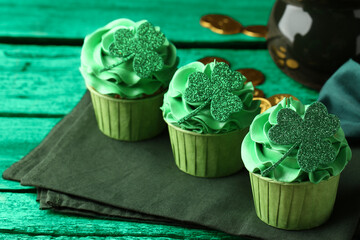 St. Patrick's day. Tasty cupcakes with clover leaf toppers and cream on green wooden table, closeup