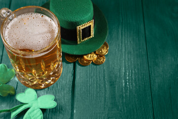 St. Patrick's day. Beer, leprechaun hat, gold and decorative clover leaves on green wooden table....