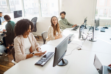 Obraz premium A team of professionals works in a brightly lit open space office. The diverse group is focused on their computer screens, suggesting a collaborative and tech-savvy workplace