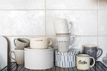 Gray and white cups with hearts and the inscription - I love you on a shelf in the kitchen against the background of a gray tiled wall.