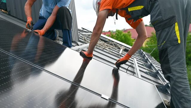 Workers building photovoltaic solar panel system on rooftop of house. Men technicians installing solar module with help of hex key outdoors. Alternative and renewable energy generation concept.