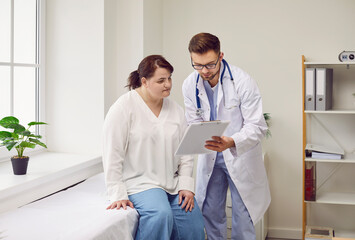 Doctor and patient talking about medical examination at clinic. Man physician shows clipboard with...