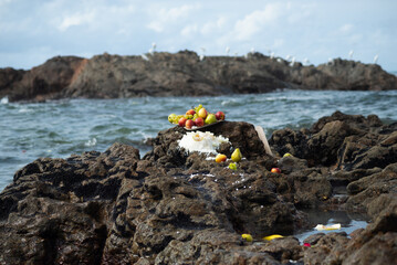 Food vase with fruits on top of a beach rock. Religious tribute.