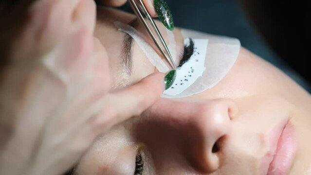 Close-up of eyelash extension procedure. Work process of a professional beauty technician lengthening women's eyelashes. False eyelashes. Eyelash extensions close-up. 