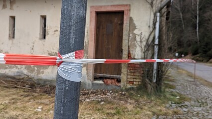 Absperrband am Pfahl vor marodem Abriss Haus