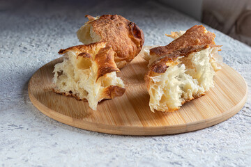 Fresh bread, broken into pieces, lies on round cutting board. Simple healthy food has wonderful look and taste