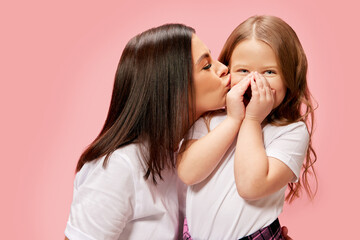 Beautiful, caring young woman, mother kissing her cute tender little girl, daughter against pink...