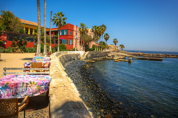 Seaside dining setup with colorful tablecloths on Goree Island, Senegal, overlooking calm waters...