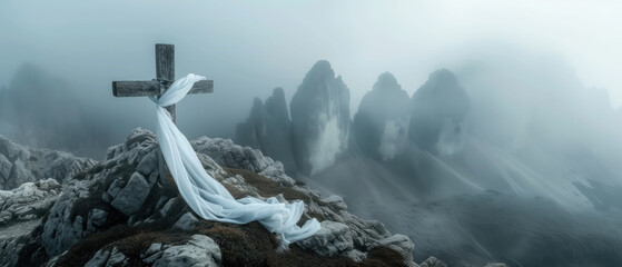 White satin scarf tied around weathered wooden cross on top of a windswept mountain peak overlooking a range of jagged, rocky peaks partially obscured by mist. - obrazy, fototapety, plakaty