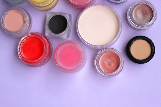 Bowls with various colorful cream beauty products on purple background. Top view.