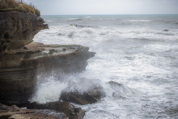 waves breaking on stones of truman track in new zealand on rainy day