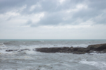 Fototapeta na wymiar waves breaking on stones of truman track in new zealand on rainy day