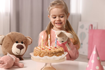 Obraz na płótnie Canvas Cute girl with birthday cake and toys at table indoors