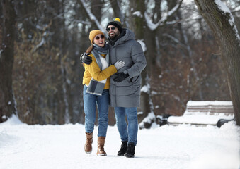 Fototapeta na wymiar Happy young couple walking in snowy park on winter day