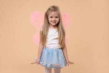 Cute little girl in fairy costume with pink wings on beige background