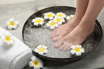 Obraz na płótnie Canvas Woman soaking her feet in bowl with water and flowers on light grey floor, closeup. Spa treatment