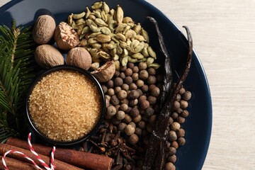 Naklejka premium Plate with different aromatic spices and fir branches on light wooden table, top view