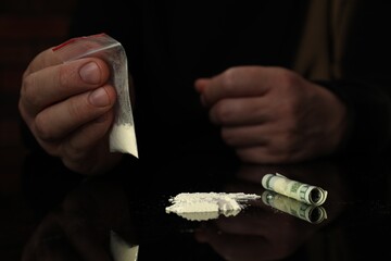 Drug addiction. Man with cocaine and rolled dollar banknote at black table, closeup