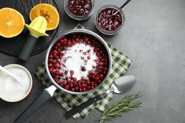 Making cranberry sauce. Fresh cranberries with sugar in saucepan and ingredients on gray table, flat lay. Space for text