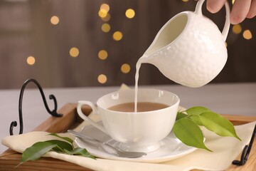 Woman pouring milk into cup with aromatic tea at table, closeup