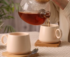 Woman pouring aromatic tea into cup at table, closeup