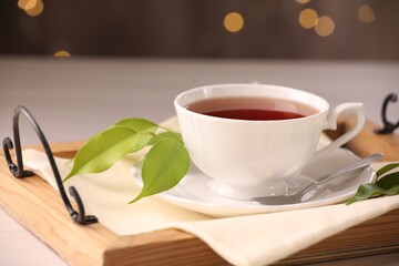 Aromatic tea in cup, saucer, spoon and green leaves on table