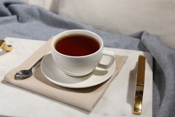 Aromatic tea in cup, saucer and spoon on table