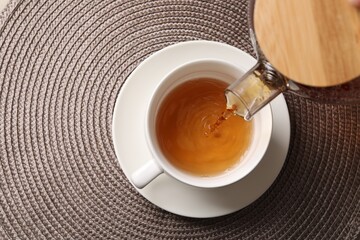 Pouring aromatic tea into cup at table, top view. Space for text