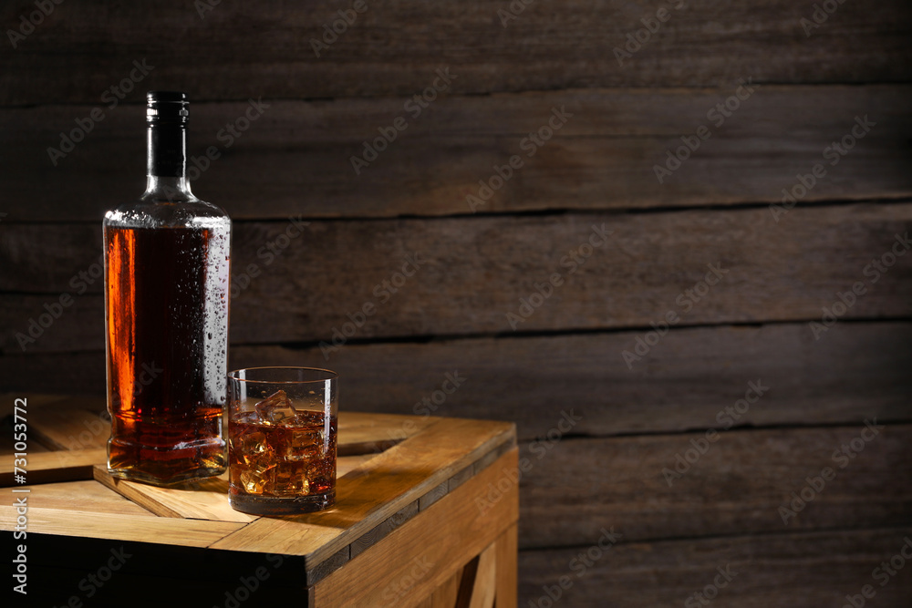 Wall mural Whiskey with ice cubes in glass and bottle on wooden crate, space for text