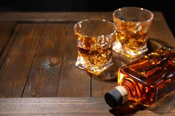 Whiskey with ice cubes in glasses and bottle on wooden crate, closeup. Space for text