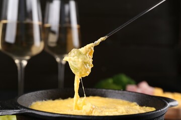 Dipping grape into fondue pot with melted cheese on table, closeup