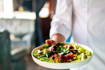 Men's chef or waiter hands hold a Roastbeef salad with vegetables on plate