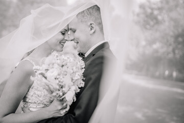 Valmiera, Latvia - July 7, 2023 - Bride and groom in close embrace, faces touching under the veil,...