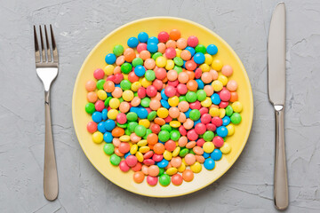 cutlery on table and sweet plate of candy. Health and obesity concept, top view on colored background