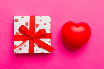 gift box with red bow and red heart on colored background . Top view. Flat lay