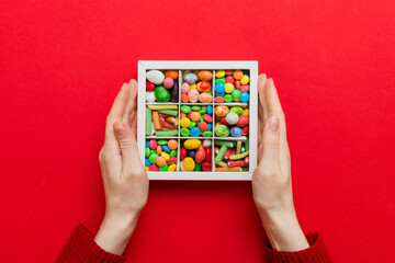 Female hands with delicious candies in box on color background
