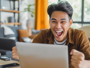 A young Indonesian male in his 20s looking at his laptop screen with a smile and joy