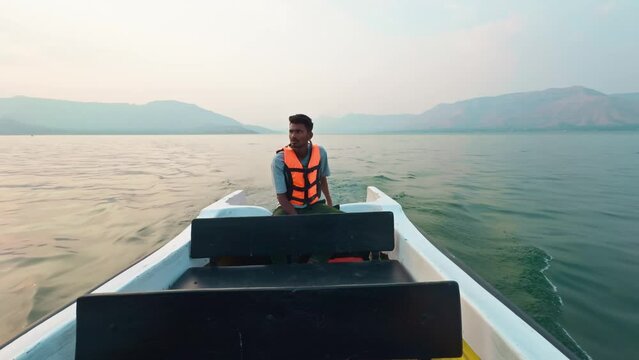 Smiling fisher man wearing a life jacket sitting on a speed boat talking with guest a serene sea or lake and hills in the background at dusk