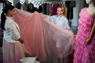 Young fashion designer demonstrates pink evening dress to client