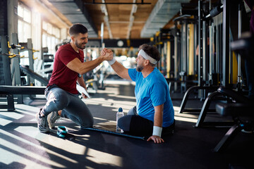 Happy coach congratulating mature man on successful exercise class in gym.