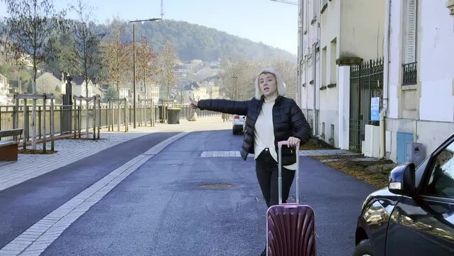 Girls with pink suitcase stops a taxi on the street 