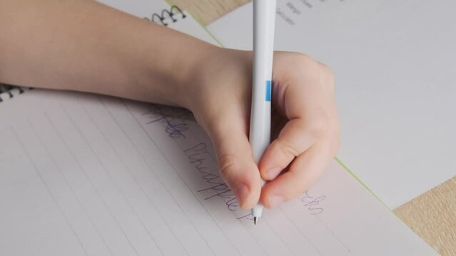 left-handed schoolchild doing homework, child writes English in notebook, assignments involving English language exercises, acquisition, vocabulary building in school setting, Bilingual Education