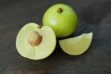 Closeup of Fresh Amla Berry Cross Section with Whole Fruit on Black Wooden Background
