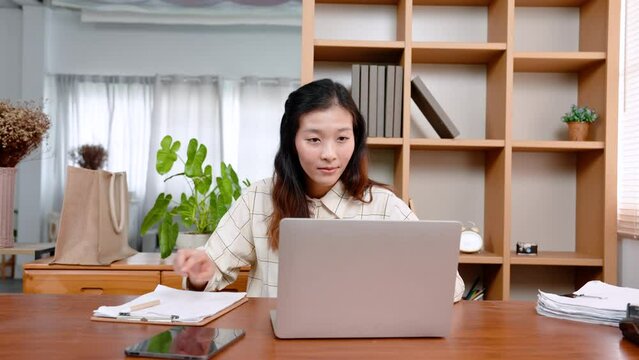 Asian female office worker, sitting signing documents related company work, was assigned project, when finished, turned around and returned work, continuing typing on laptop computer.