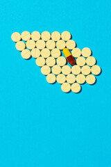 Capsule pill surrounded with yellow pills as square on blue background