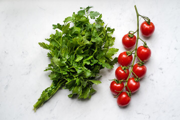 Fresh raw cherry tomatoes with bunch of parsley on a marble background, top view from above