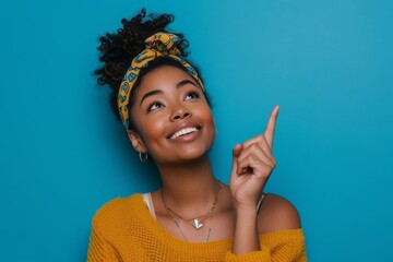 Beautiful young black woman pointing up to copy space Looking satisfied and happy Perfect for advertising products or services Isolated on a blue background